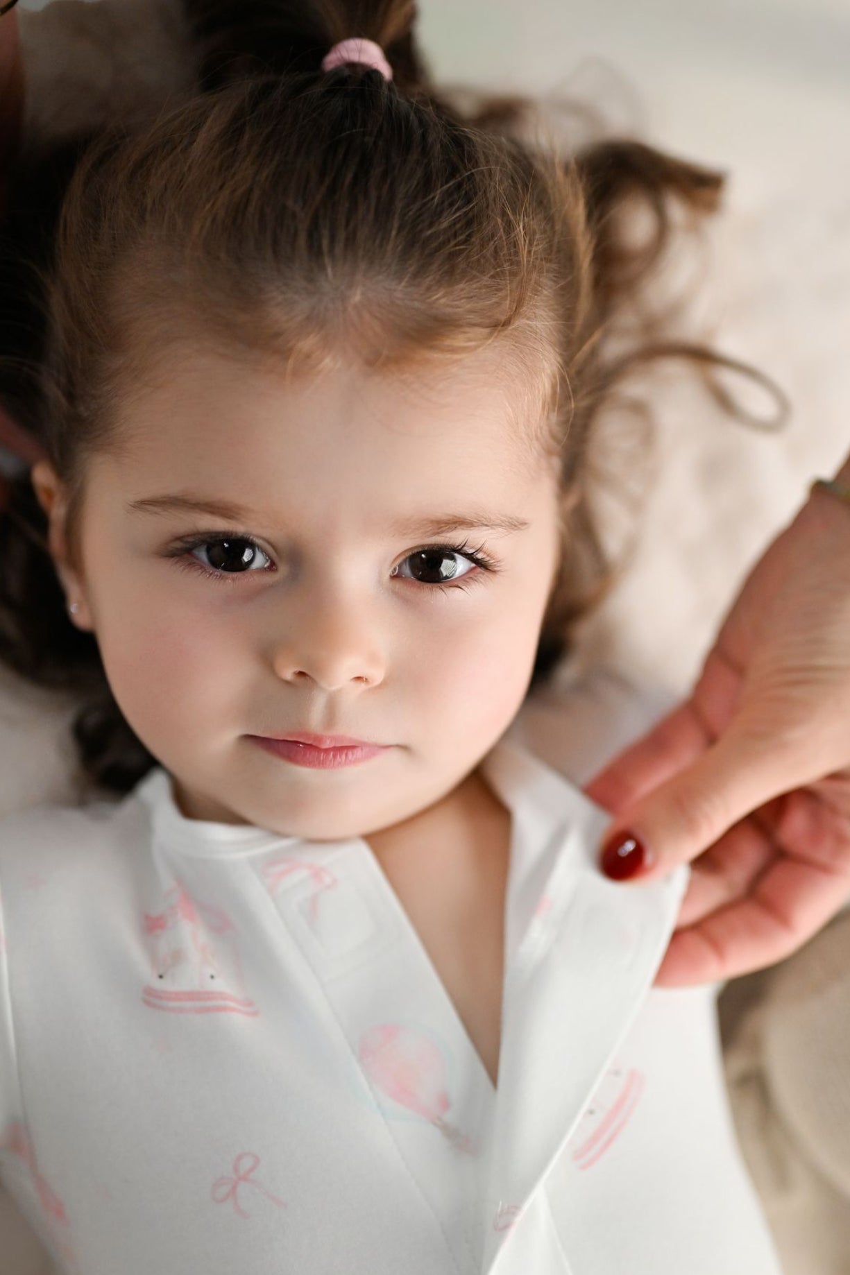 Child wearing a white outfit with pink patterns, held by an adult.